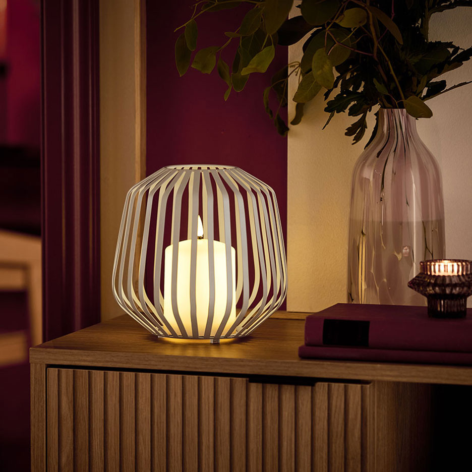 Eine LED-Kerze in einem weißen Metallhalter auf einer Holzkommode.