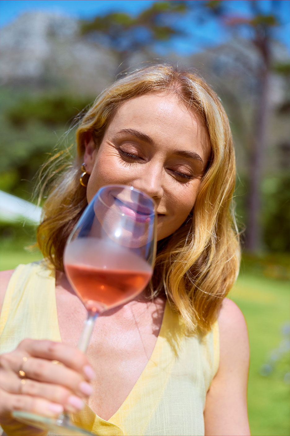 Lächelnde Frau genießt ein Glas Roséwein im Freien.