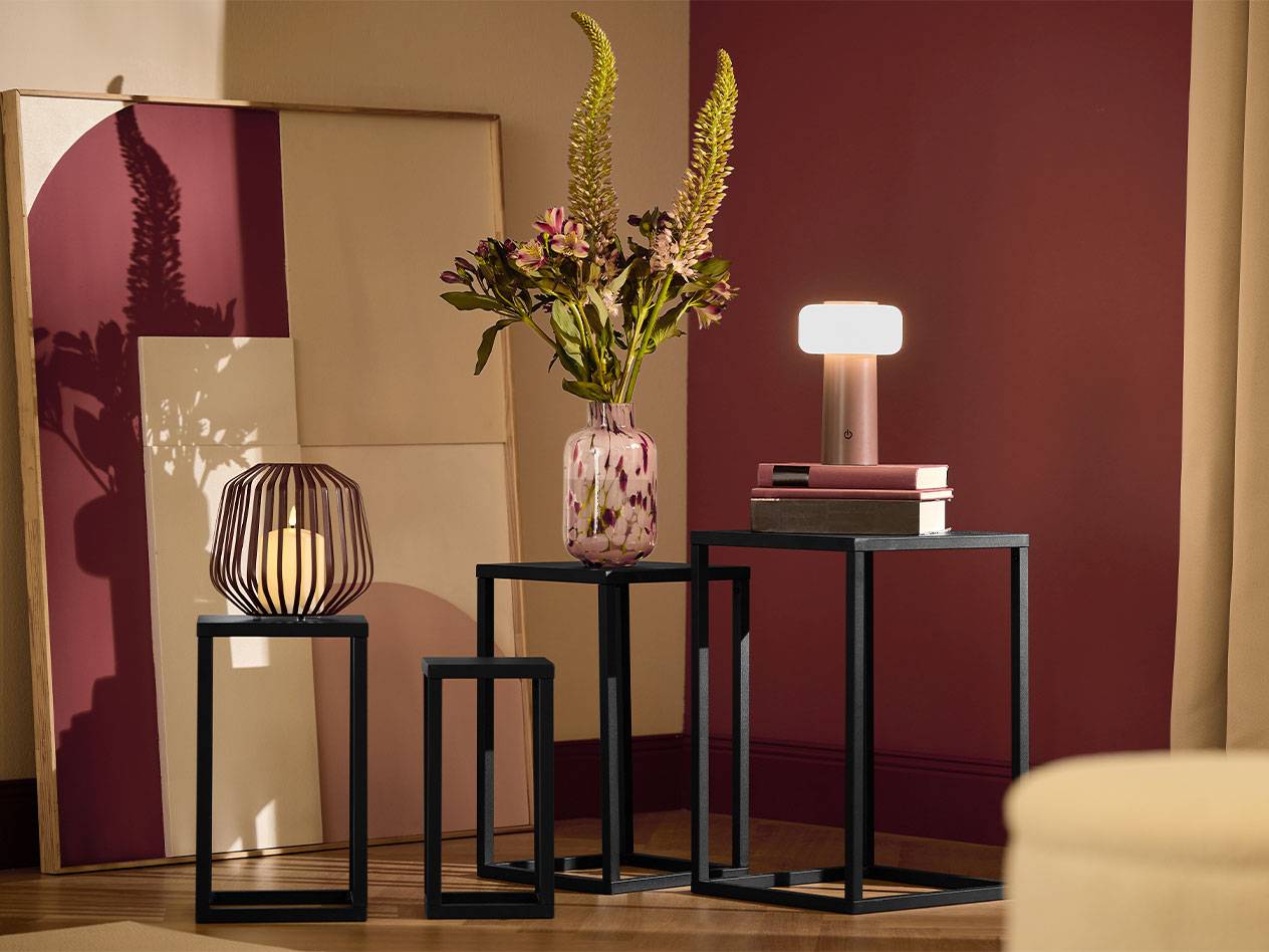 Drei schwarze Beistelltische mit einer Kerze, einer Blumenvase und einer Lampe.