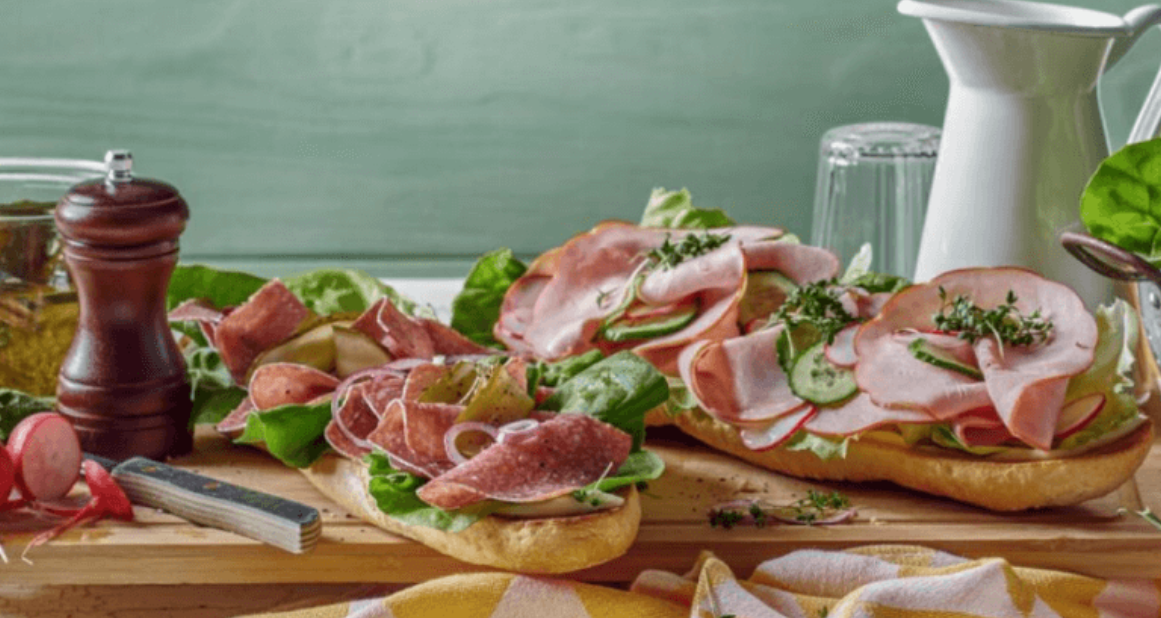 Zwei belegte Baguettes mit Wurst, Salat und Gemüse auf einem Holzbrett.