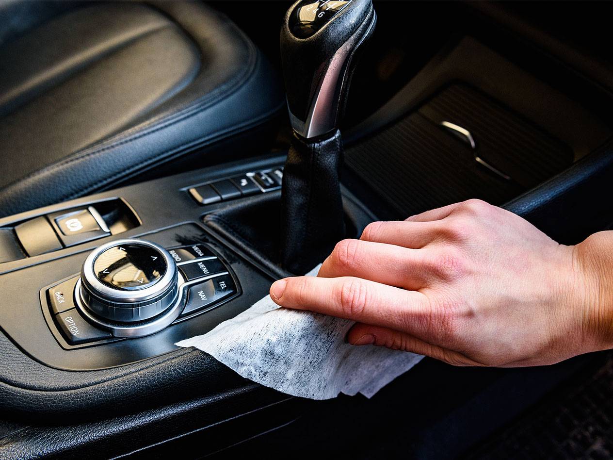 Hand reinigt das Autointerieur mit einem Feuchttuch.