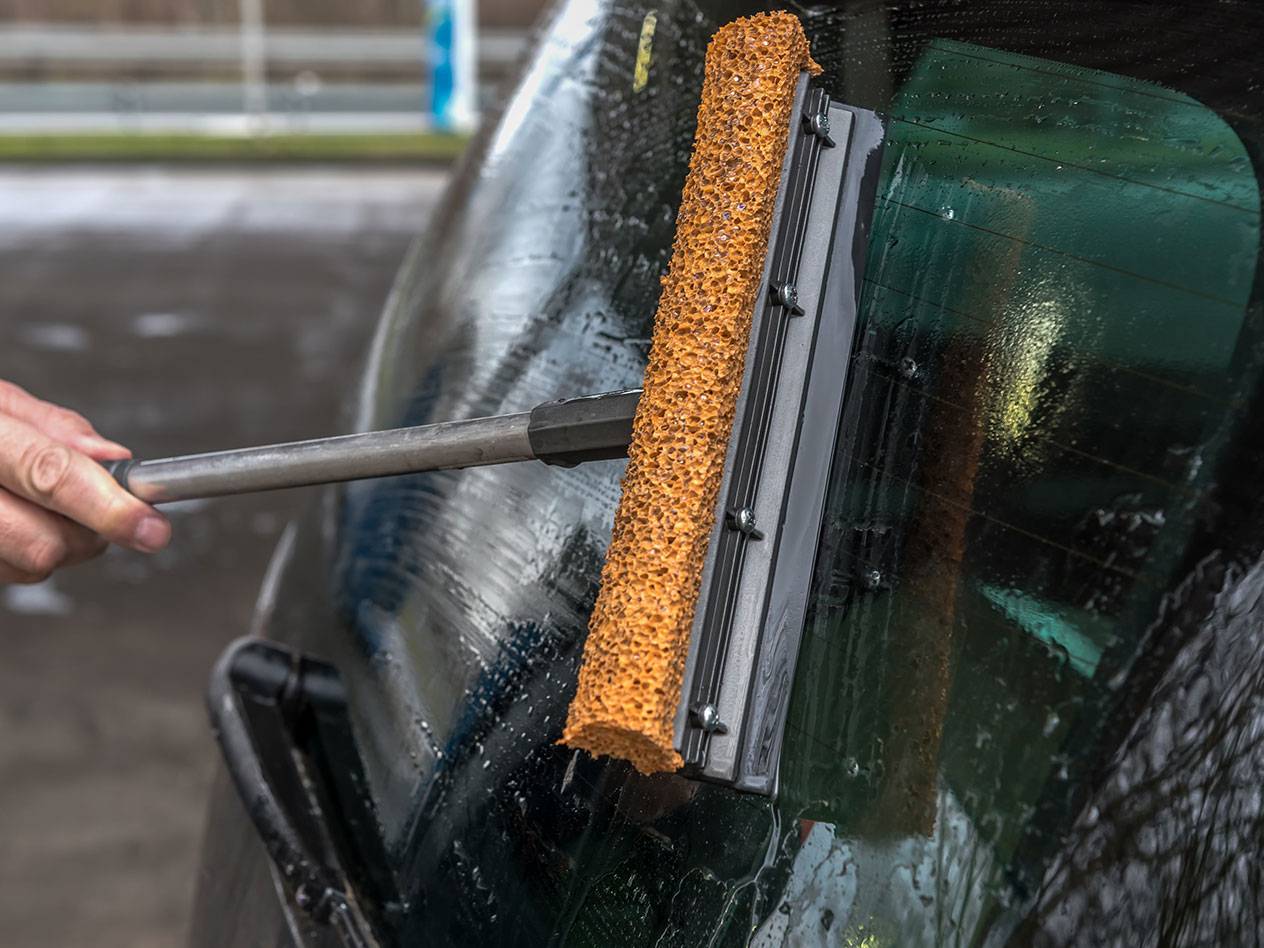 Fensterwischer mit langem Griff reinigt die Heckscheibe eines Autos.