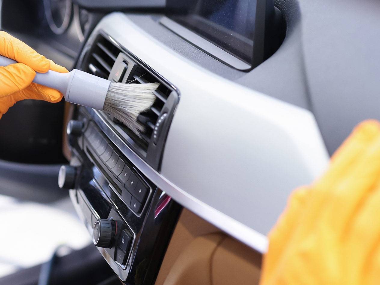 Reinigung des Autoinnenraums mit einer Detailbürste und Gummihandschuhen.