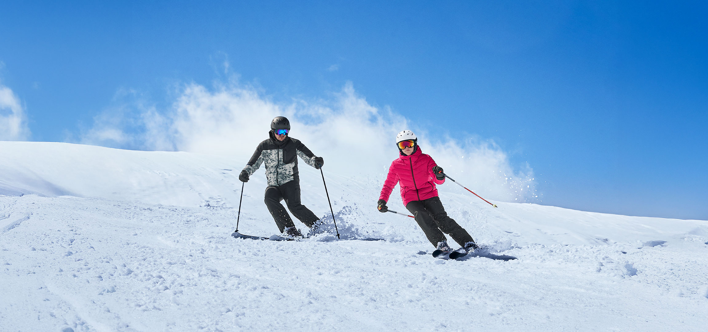 Zwei Skifahrer in Skibekleidung und Skiausrüstung auf einer verschneiten Piste.