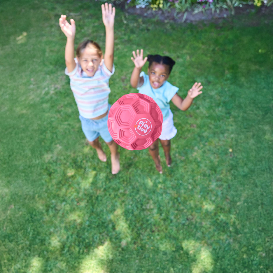 Zwei Kinder spielen draußen mit einem rosa Ball.