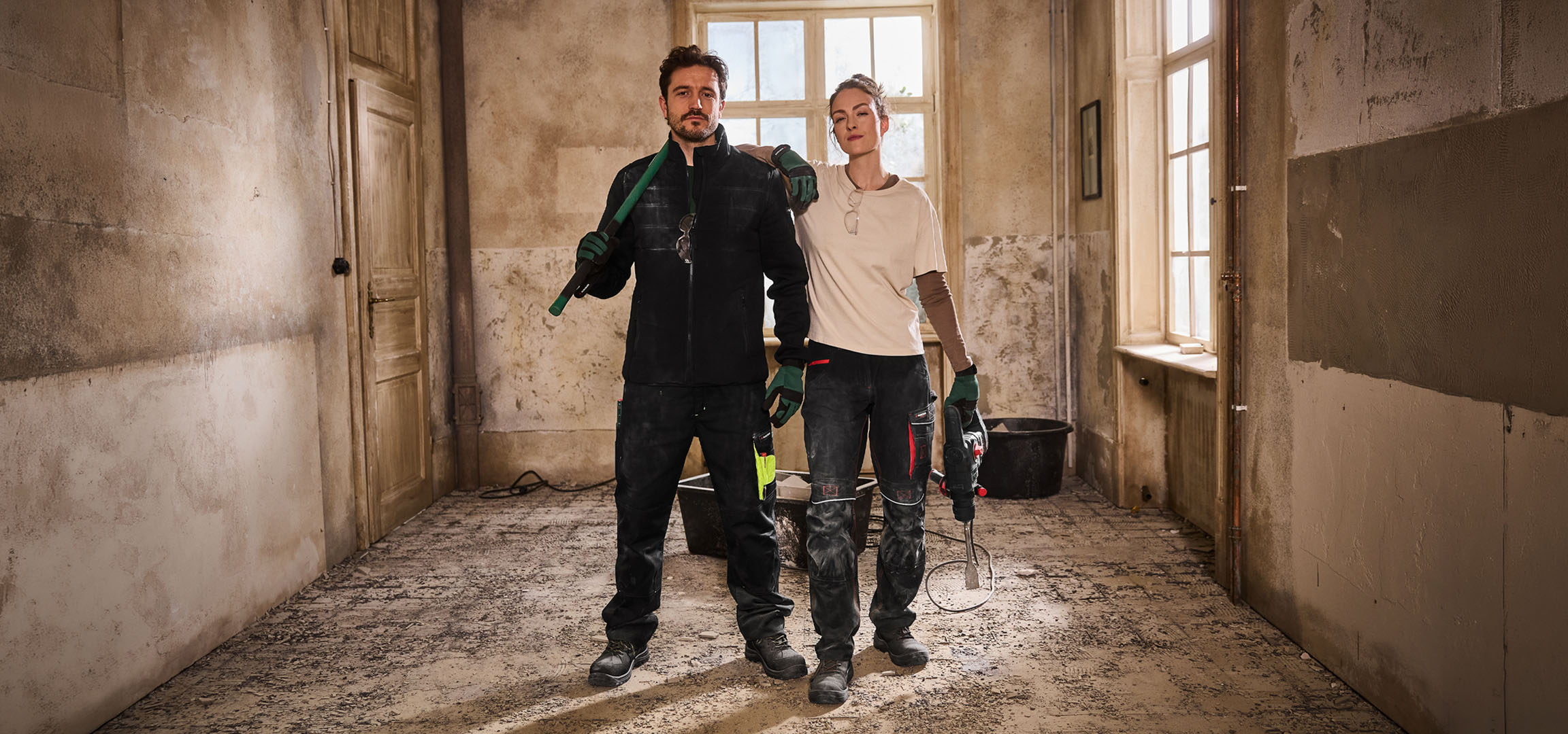 Zwei Bauarbeiter in Arbeitskleidung mit Werkzeugen auf einer Baustelle.