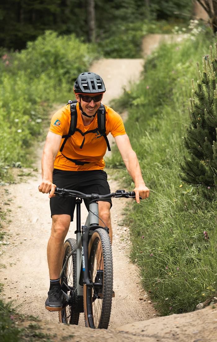 Ein Mann lächelt, während er mit dem Mountainbike auf einem Trail fährt.