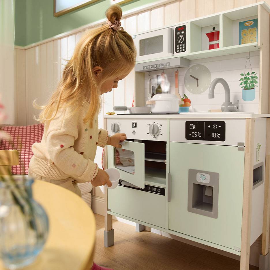 Kind spielt mit einer Holzküche, mit Backofen, Mikrowelle und Kühlschrank.