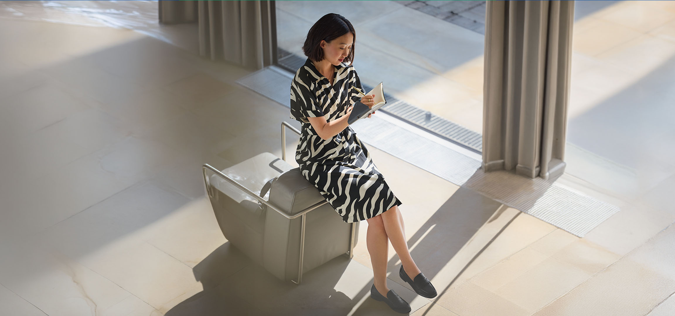 Frau in Zebra-Kleid, auf einem Stuhl sitzend, in ein Notizbuch schreibend.