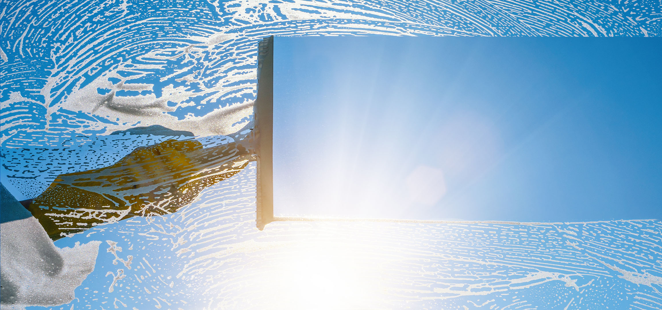 Fensterreinigung mit Seifenschaum vor blauem Himmel.