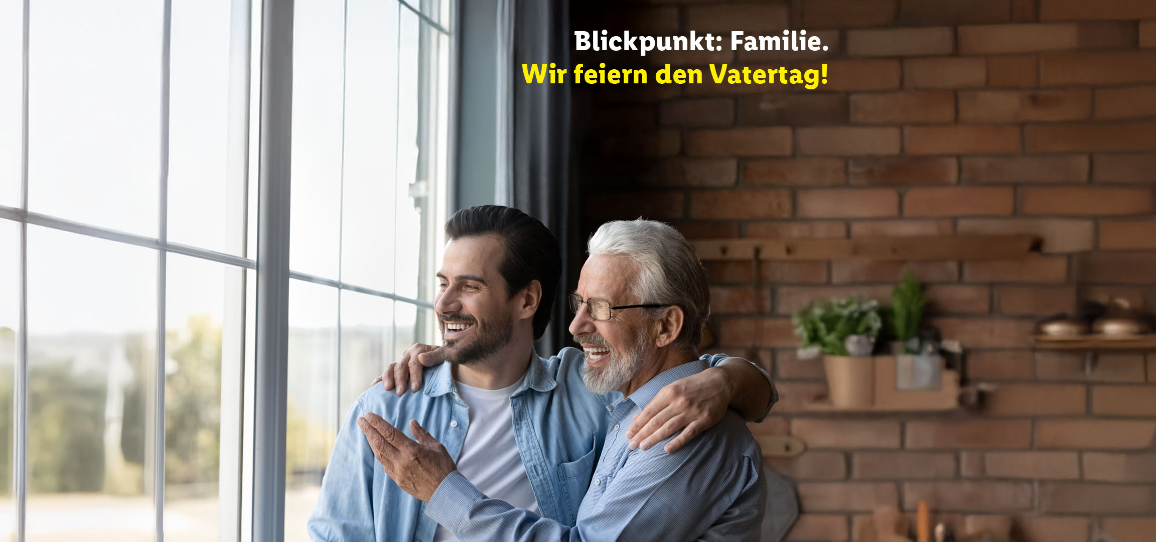 Vater und Sohn lächeln, umarmen sich am Fenster. Text: „Blickpunkt: Familie. Wir feiern den Vatertag!“