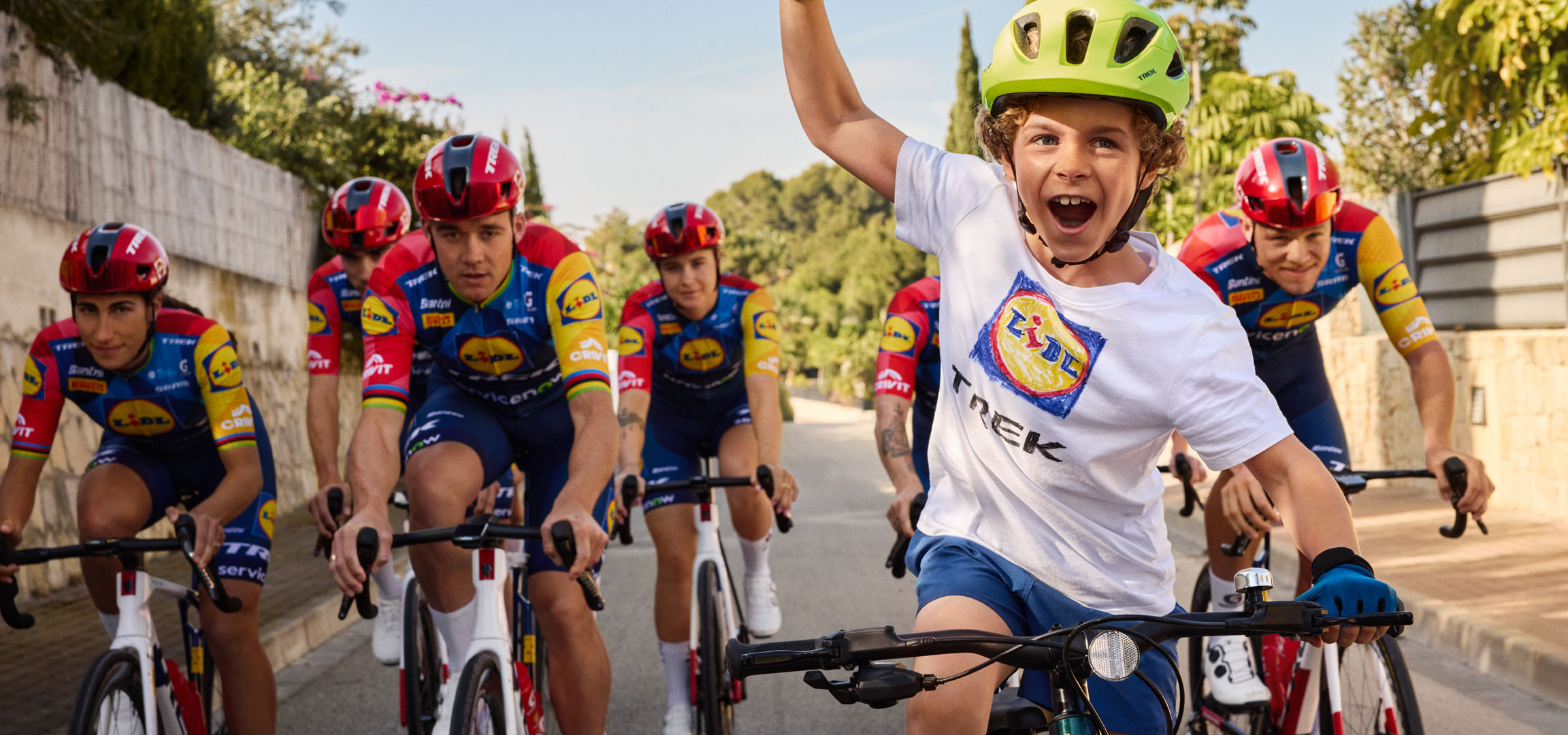 Kind mit Helm und T-Shirt mit Lidl-Logo, umgeben von Radfahrern.