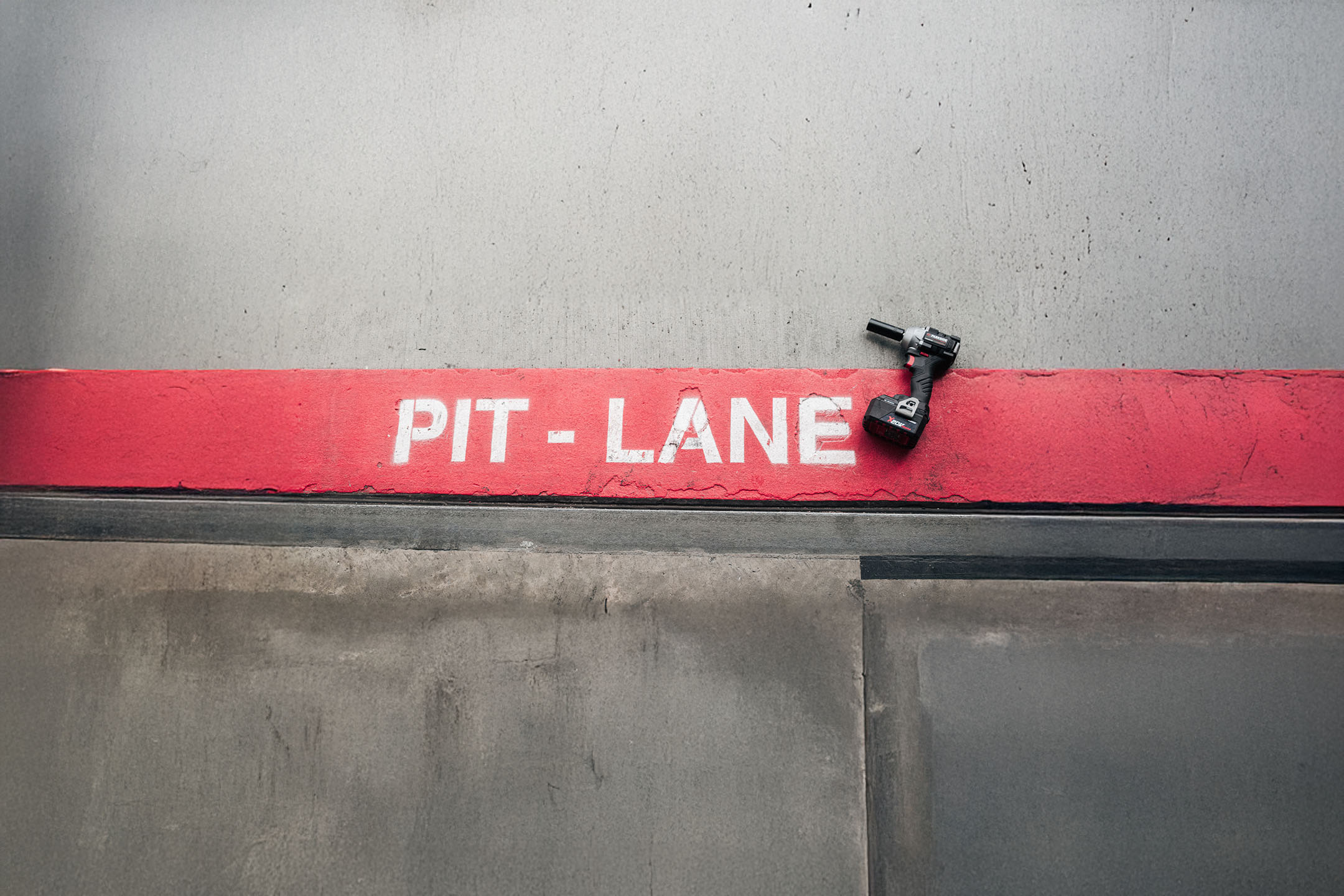 Ein Akku-Schlagschrauber auf einer roten „PIT-LANE“-Linie auf einem Betonboden.