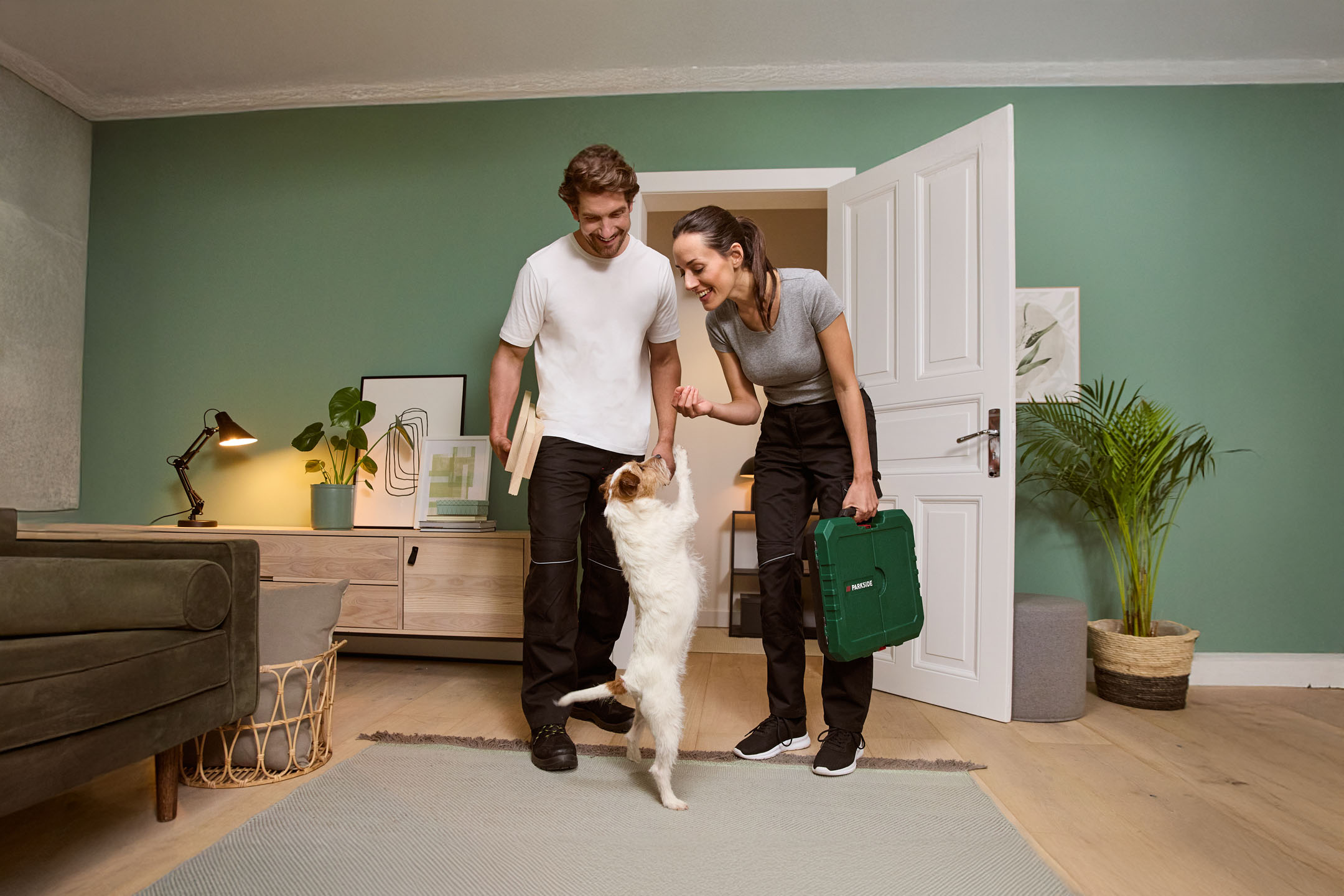 Glückliches Paar mit Hund, Werkzeugen und Heimwerkerbedarf in modernem Wohnzimmer.