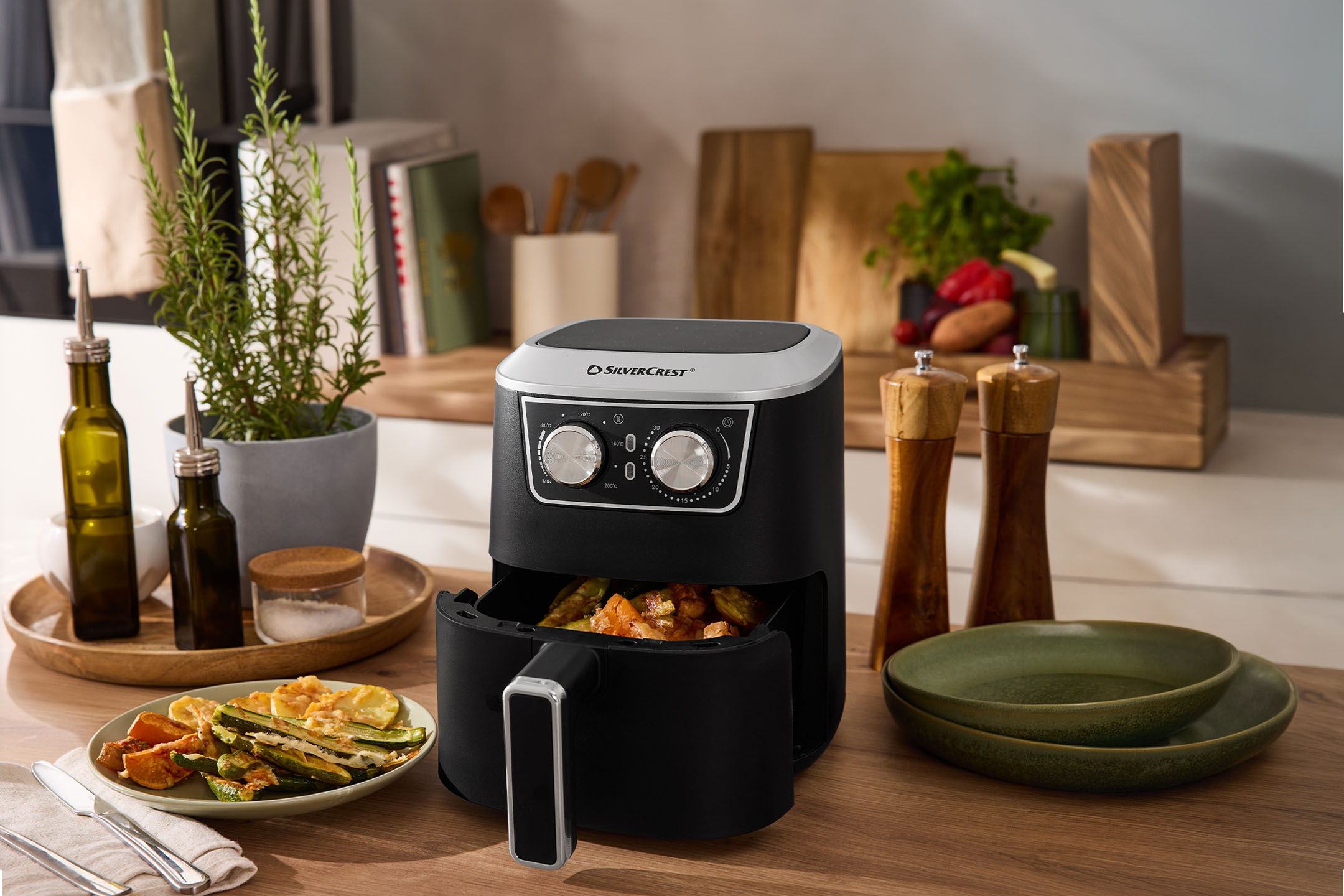 Heißluftfritteuse mit geröstetem Gemüse, Olivenöl, Salz und Pfeffer auf einer Küchenzeile.