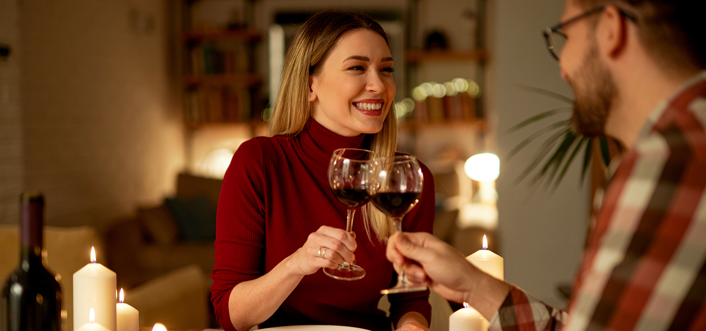 Lächelnde Frau mit Rotwein bei romantischem Abendessen bei Kerzenschein.