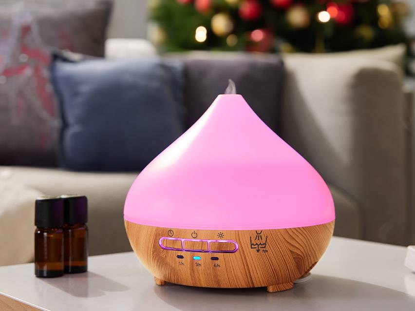 Pink leuchtender Aroma Diffusor mit Holzoptik und ätherischen Ölen auf einem Tisch.