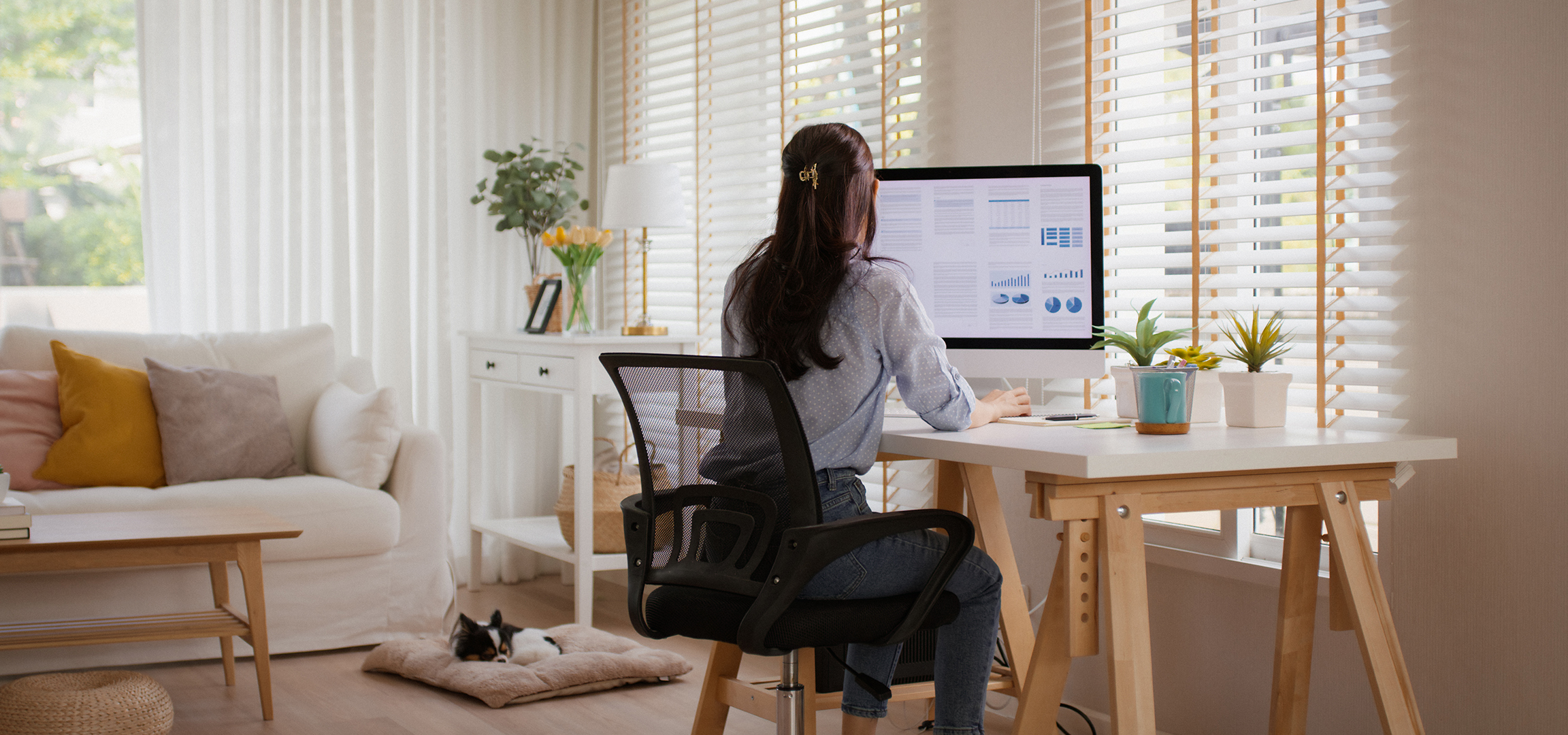 Frau arbeitet am Computer im Homeoffice, Hund schläft auf dem Boden.