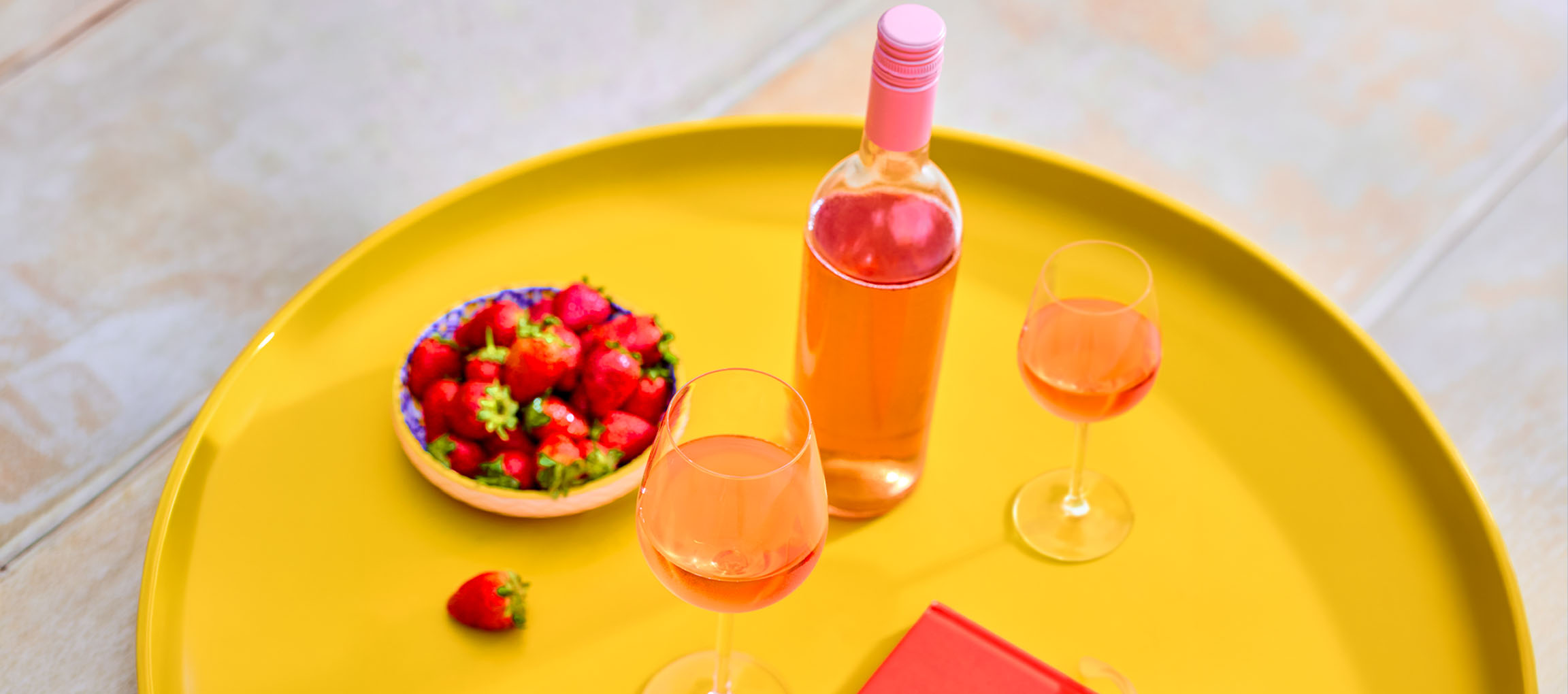 Flasche und Gläser Roséwein mit Erdbeeren auf einem gelben Tablett.