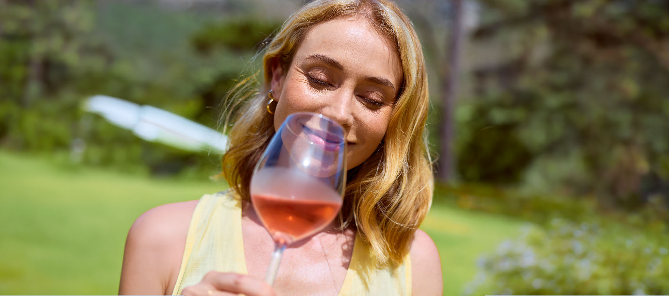 Frau genießt ein Glas Roséwein im Freien, Augen genüsslich geschlossen.