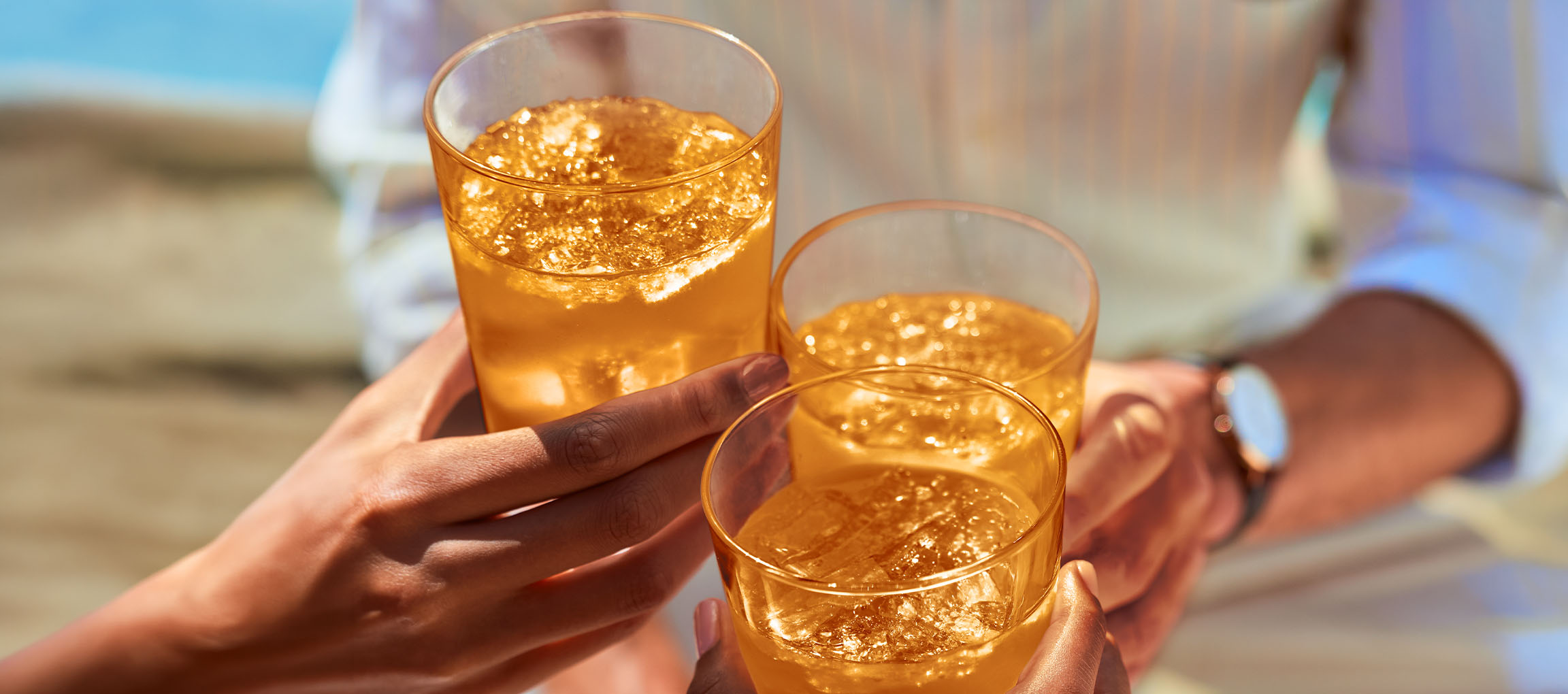 Drei Personen stoßen mit Gläsern Eistee oder Cocktails im Freien an.