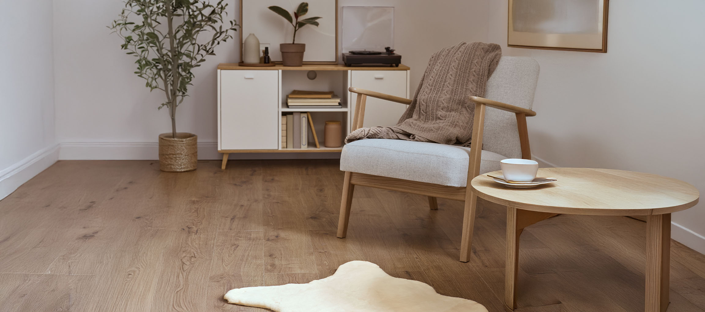 Grauer Stoff-Sessel mit Strickdecke, Couchtisch aus Holz und modernes Sideboard.