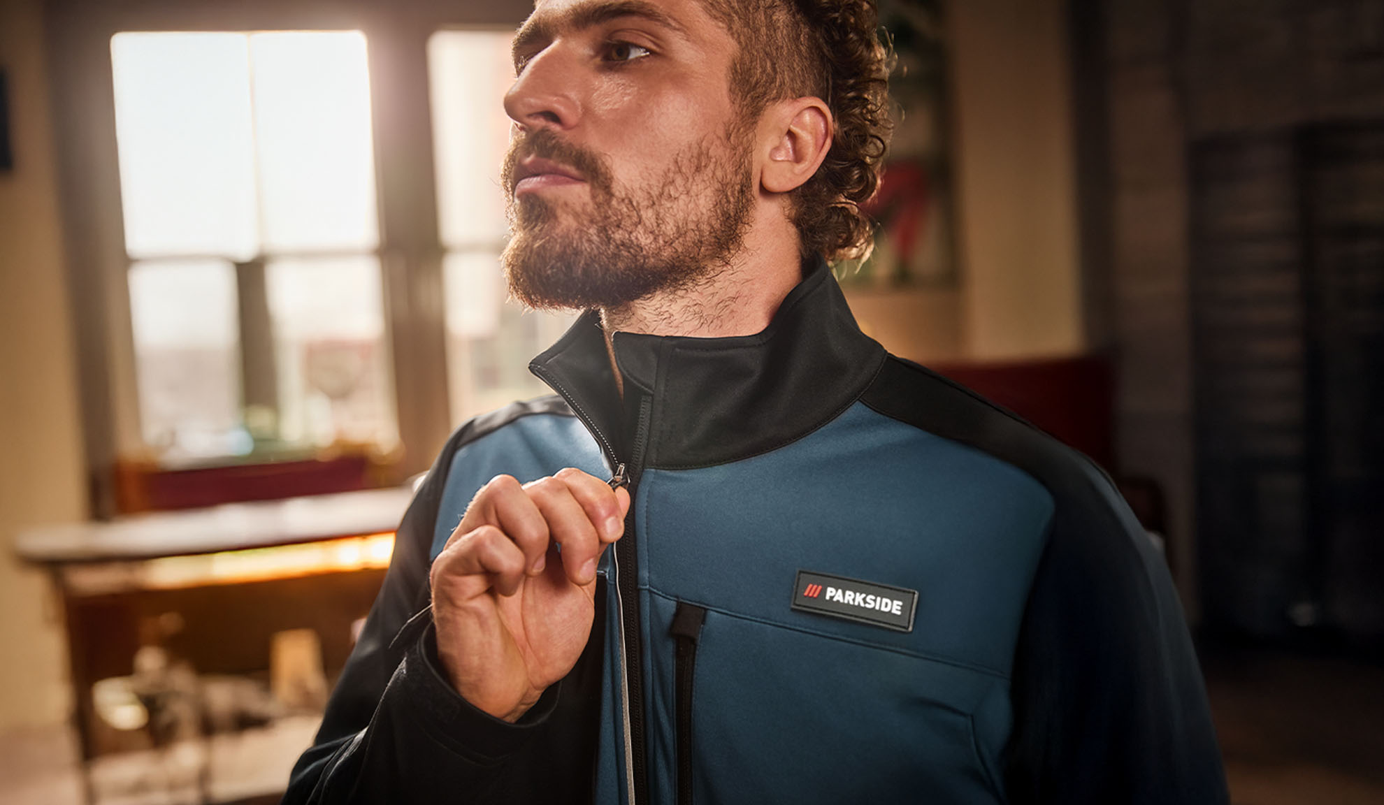 Mann in einer blau-schwarzen Parkside Arbeitsjacke, die er zuzieht.