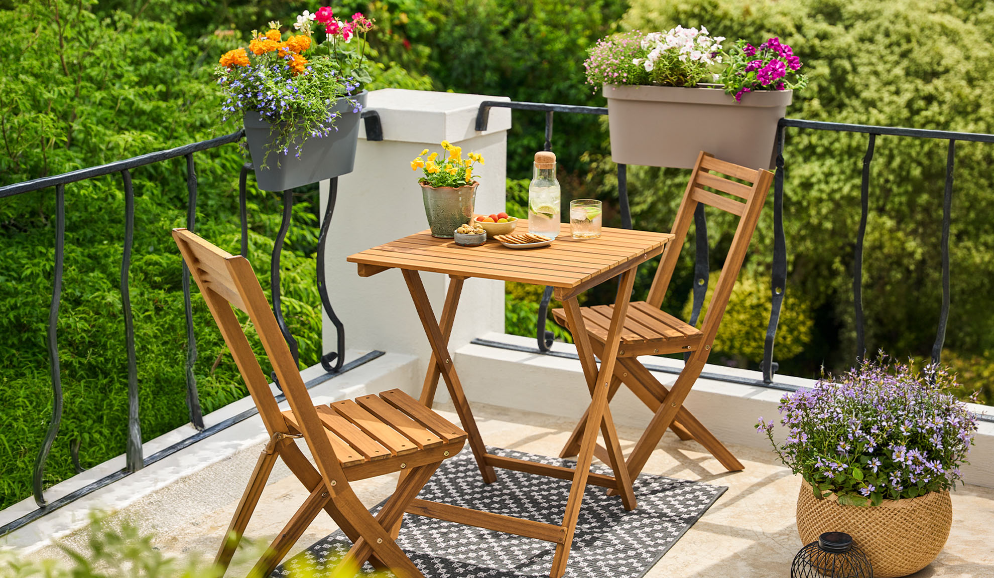 Balkon mit Holzbistro-Set, Topfblumen und Getränken auf einem gemusterten Teppich.