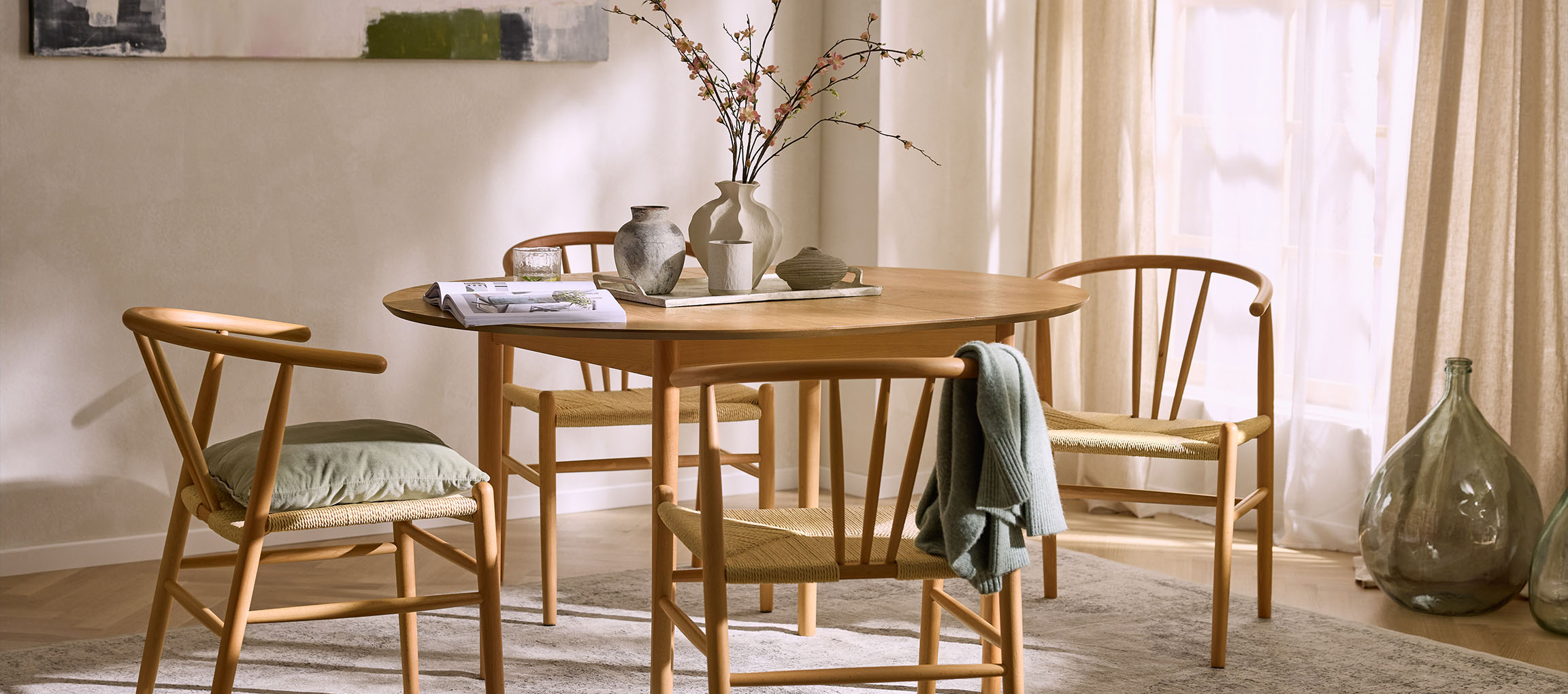 Esszimmer mit rundem Holztisch, Holzstühlen mit Seilsitzen und dekorativen Vasen.