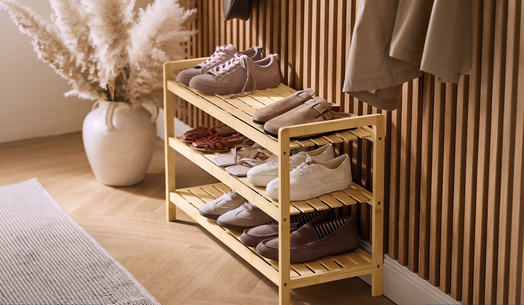 Holzschuhregal mit verschiedenen Schuhen und einer Pampasgrasvase im Flur.