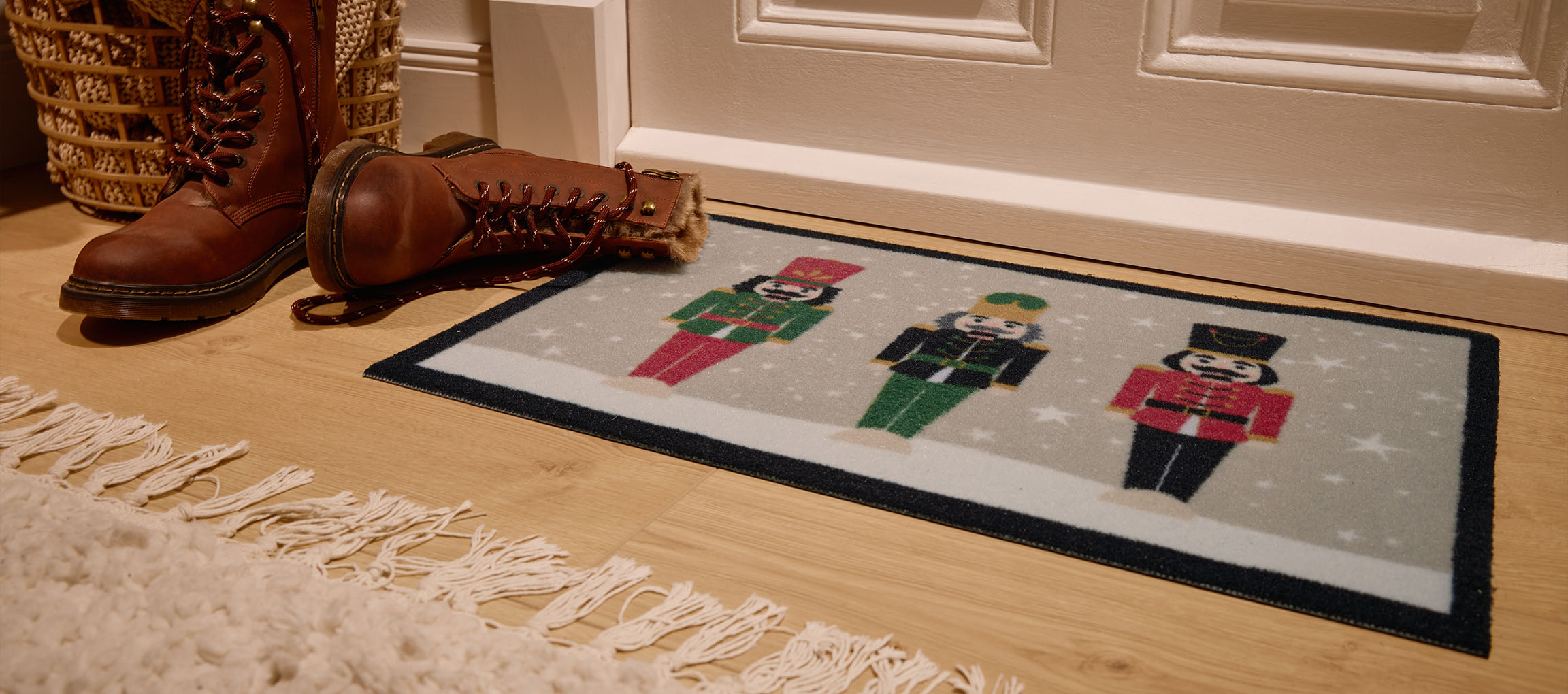 Weihnachtliche Fußmatte mit Nussknackern, braune Stiefel und Weidenkorb am Eingang.