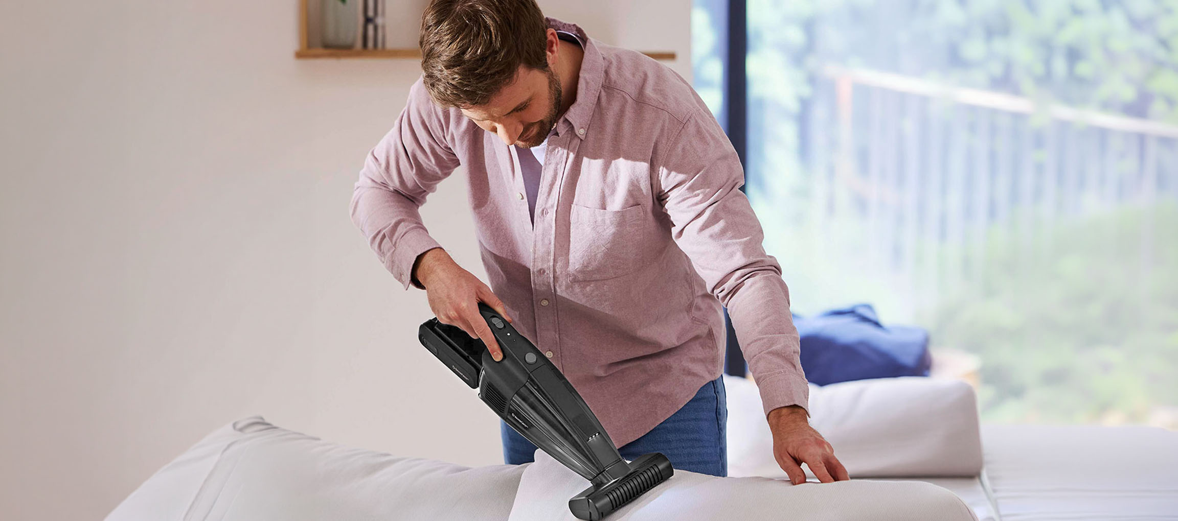 Mann reinigt Sofa mit einem Handstaubsauger.