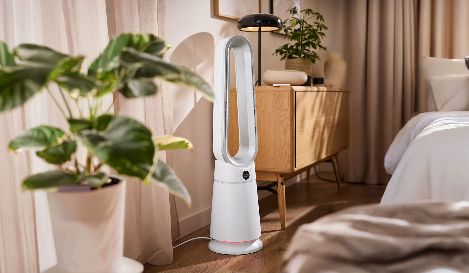 Weißer Turmventilator in einem modernen Schlafzimmer mit Pflanzen und Holzmöbeln.