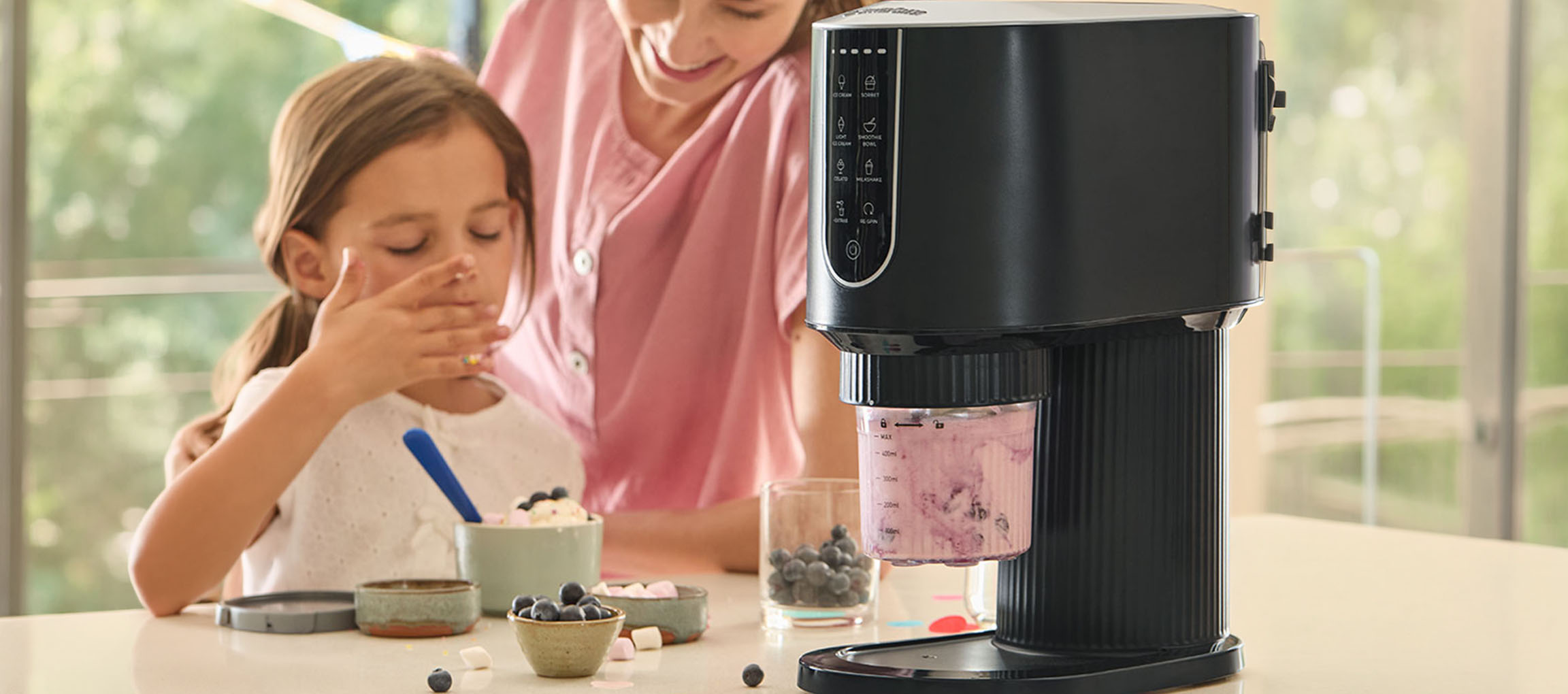 Eismaschine macht Beereneis, Kind und Erwachsener genießen das Dessert.