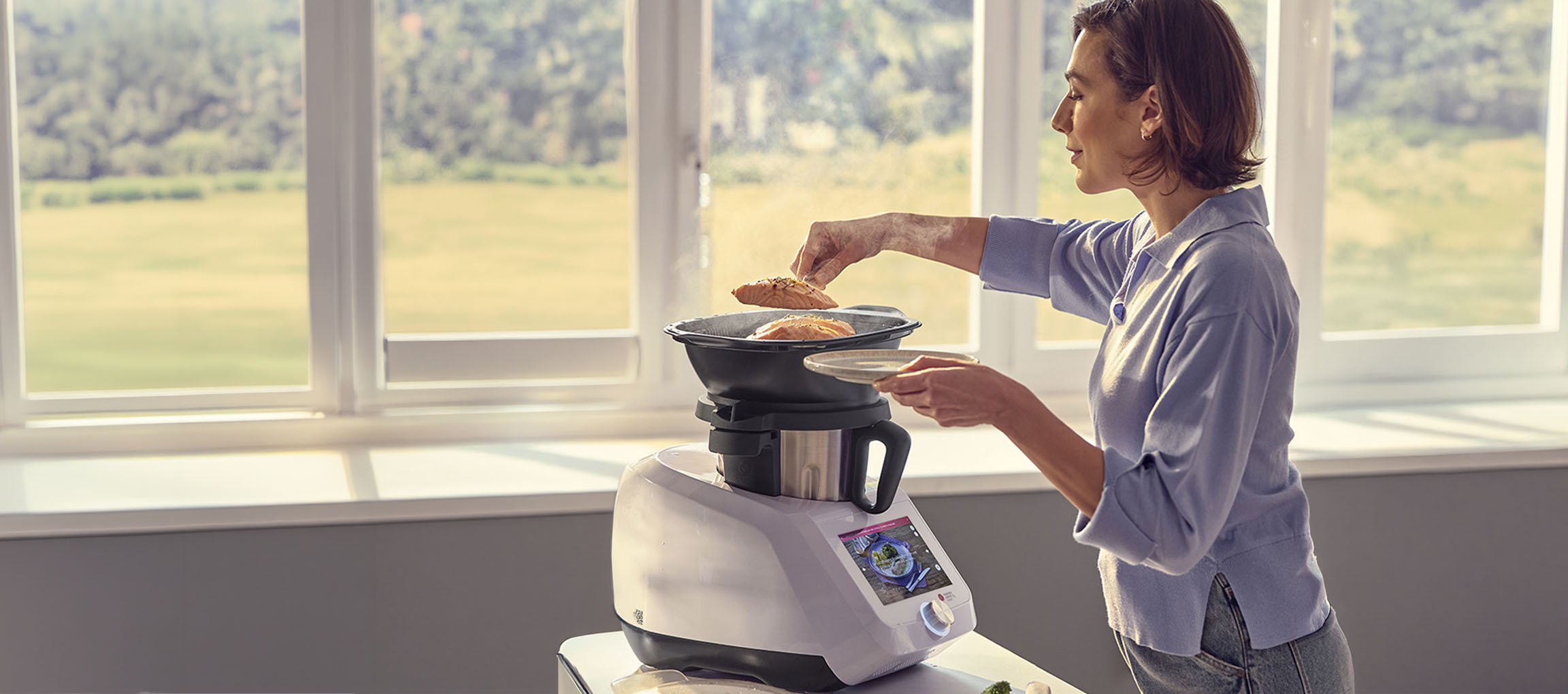 Frau kocht mit einer Küchenmaschine, mit Dampfaufsatz und Lachs.