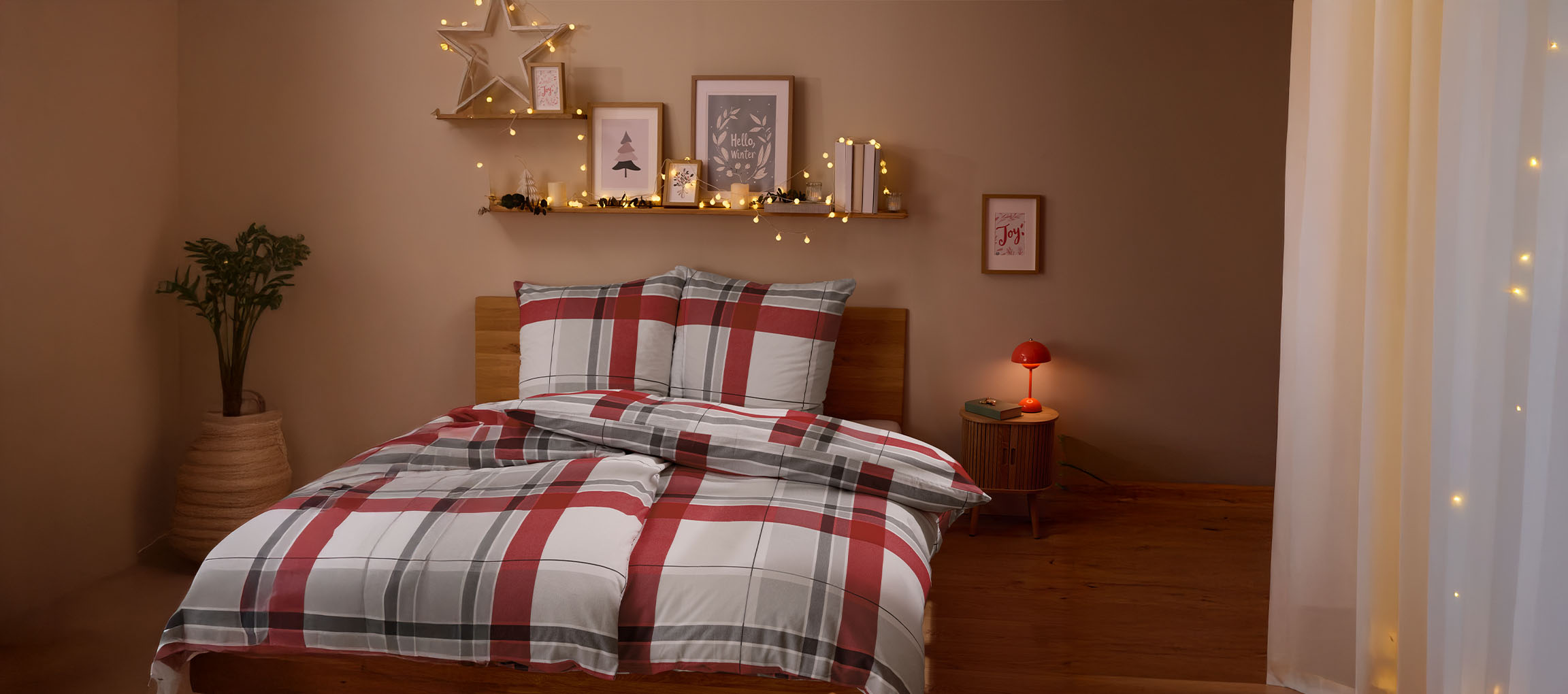 Gemütliches Schlafzimmer mit rot-grauer Karobettwäsche, Weihnachtsdekoration und Lichtern.