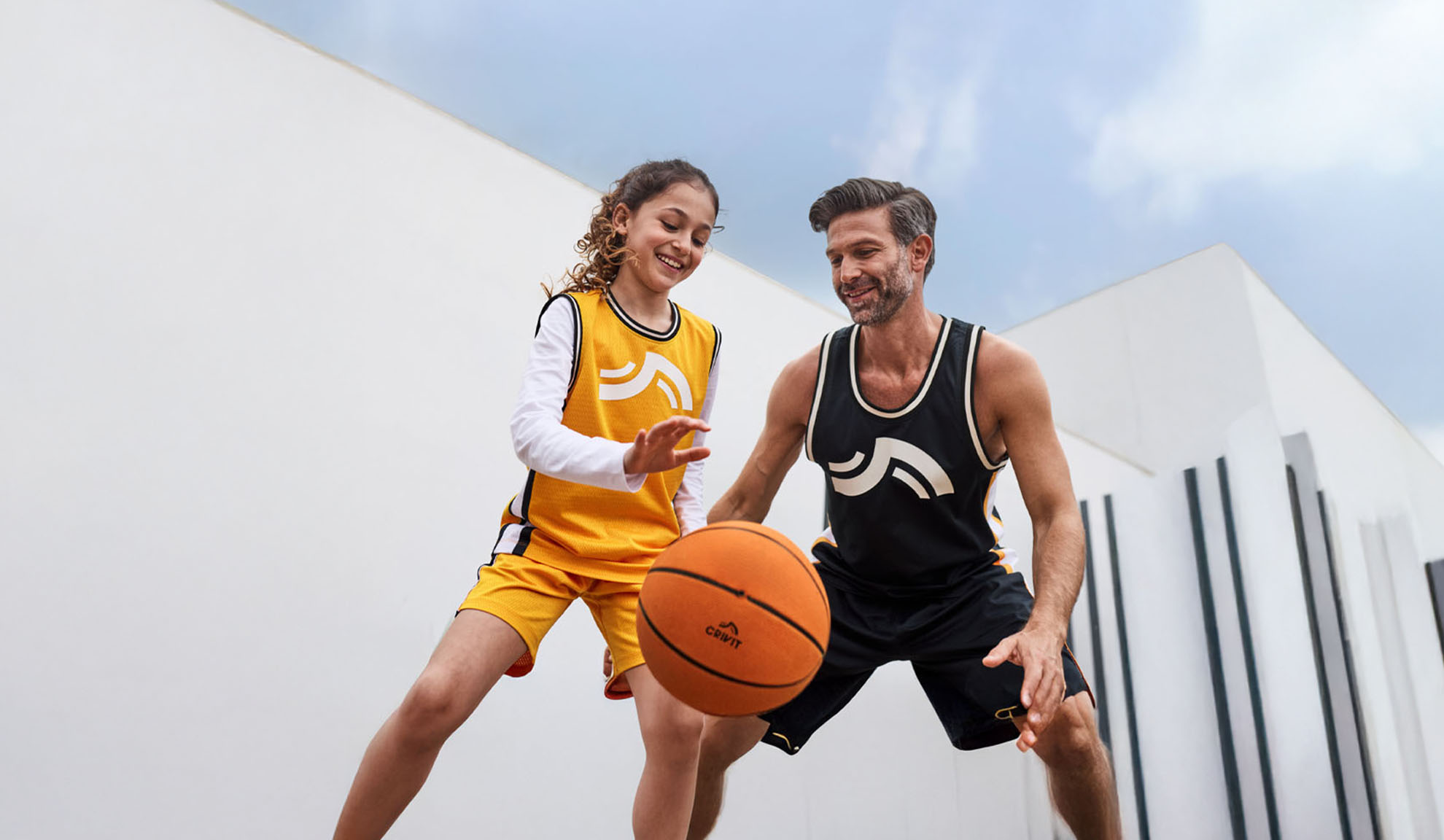Vater und Tochter spielen Basketball in Crivit Trikots und Shorts.