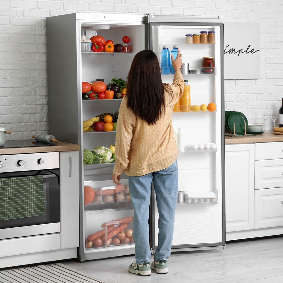Frau nimmt eine Wasserflasche aus einem Kühlschrank voller frischem Obst und Gemüse.