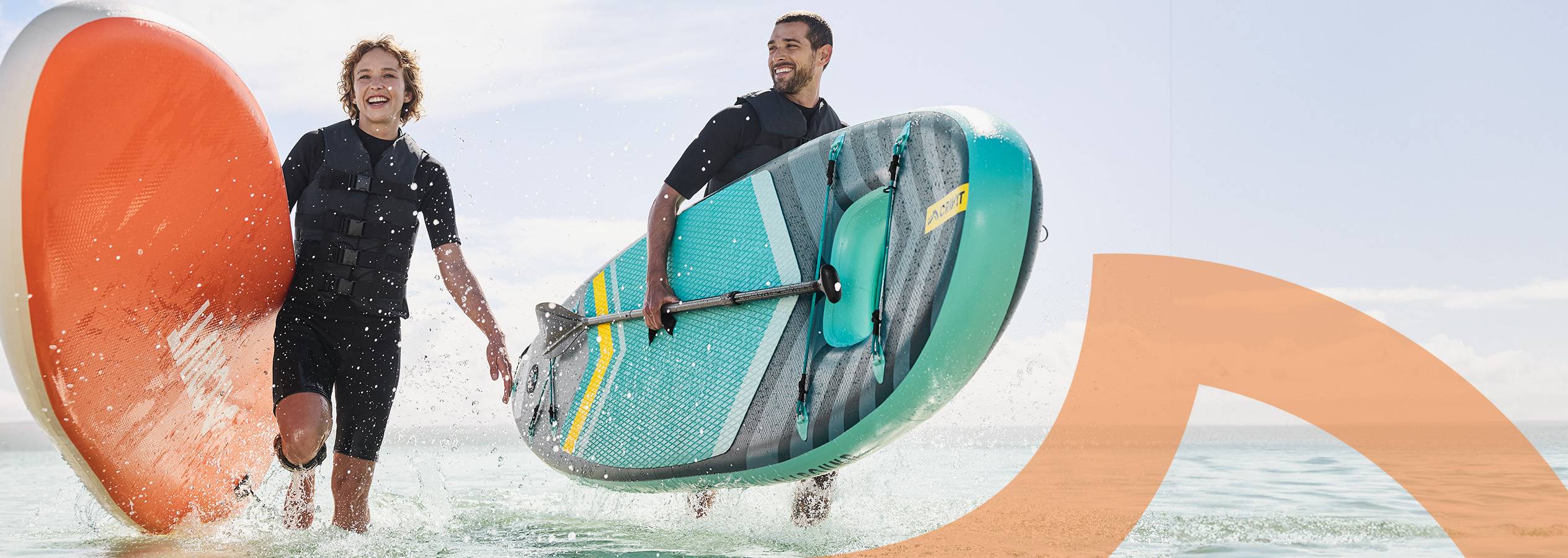 Zwei Personen mit Schwimmwesten tragen Paddleboards durch das Wasser.