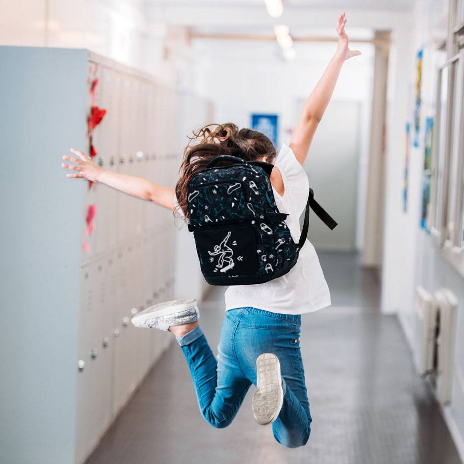Kind mit Rucksack springt in einem Schulflur.