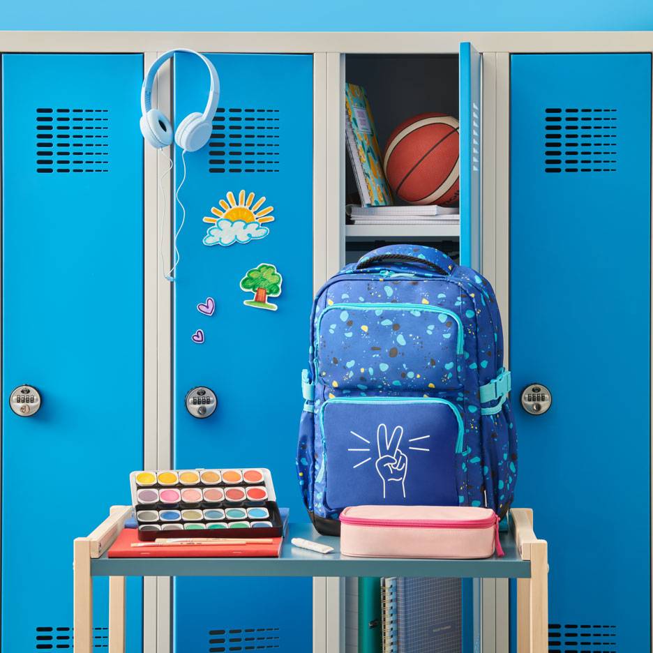 Blauer Rucksack mit Friedenszeichen, Aquarellfarben und Kopfhörern vor Schulspinden.