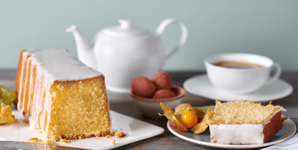 Zitronenkuchen mit Zuckerguss, Tee und Physalis auf einem Holztisch.