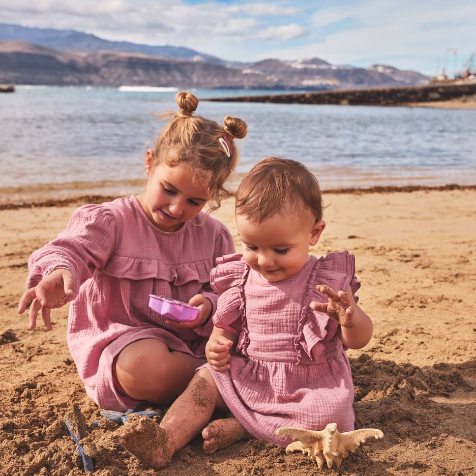 Zwei Mädchen in rosa Kleidern spielen im Sand am Strand.