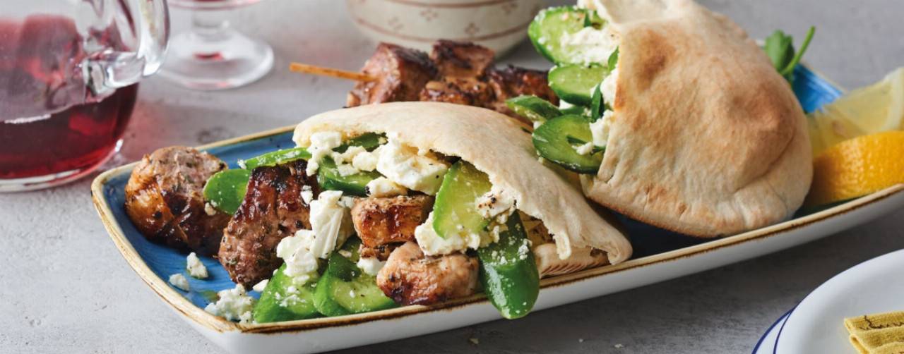 Gefüllte Fladenbrote mit Fleischspießen, Gurken und Feta auf einem blauen Teller.