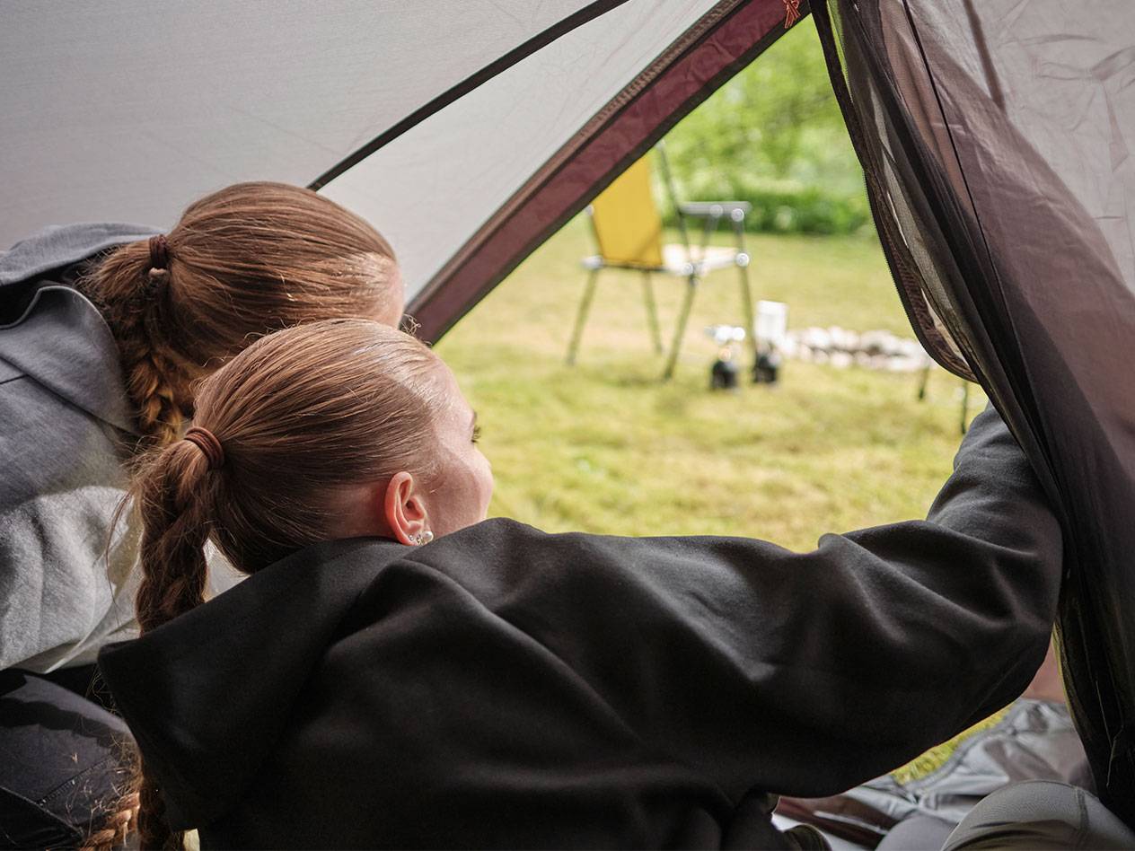 Zwei Mädchen schauen aus der Öffnung eines Zeltes.
