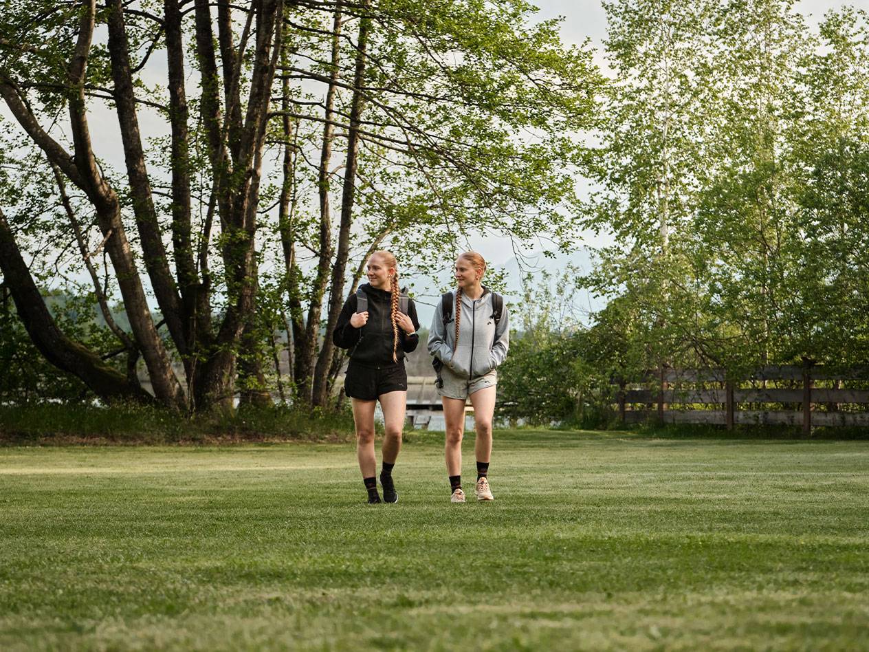Zwei Mädchen mit Rucksäcken gehen über eine Wiese.