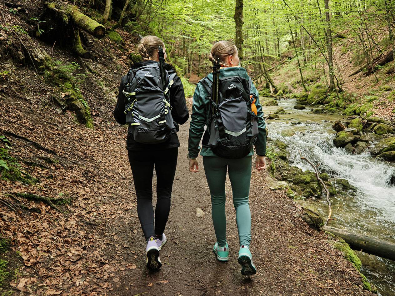 Zwei Frauen mit Crivit-Rucksäcken wandern auf einem Waldweg.