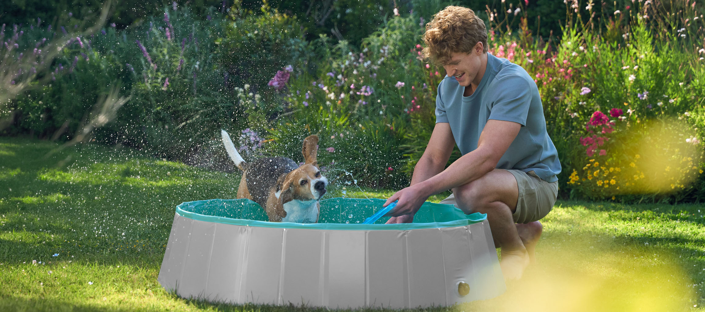 Mann und Hund spielen in einem Planschbecken im Garten.